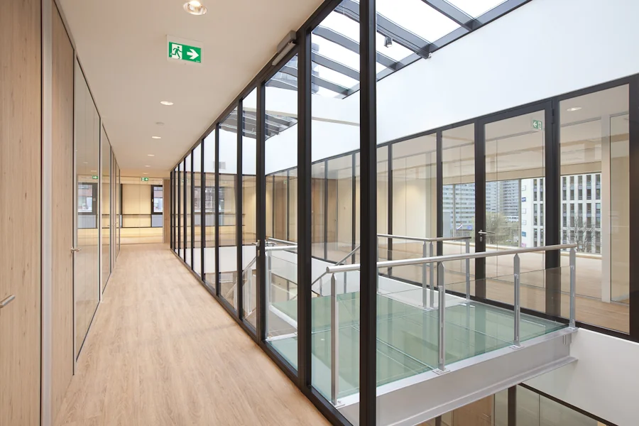 Moderne glazen loopbrug en gang in een kantoorgebouw aan de De Boelelaan met houten vloeren en veel daglicht.